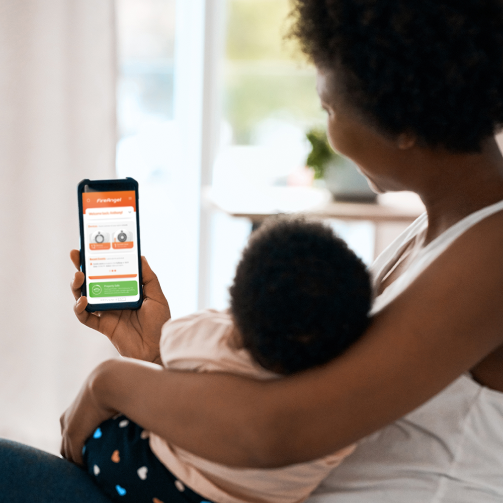 Moeder met kind bekijkt FireAngel Gateway app melding op smartphone voor brandveiligheid thuis